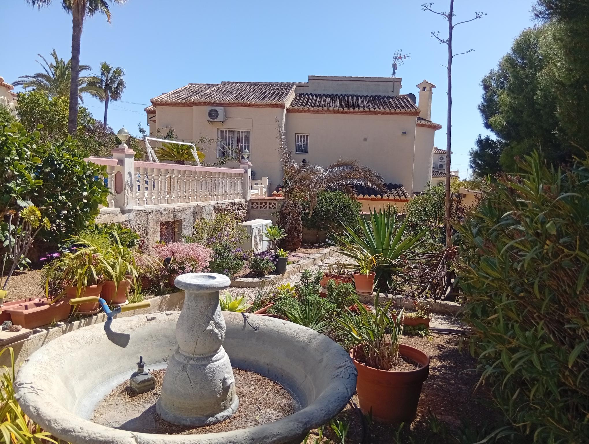 Calpe garden before redesign — overgrown front garden with pots and a bird bath.